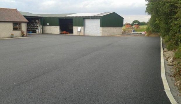 Newly surfaced commercial yard in front of green agricultural sheds