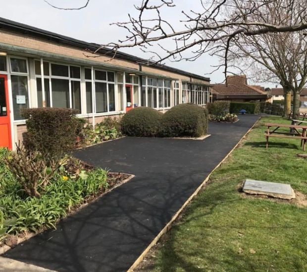 Wide tarmac walkway running along the front of a low brick building