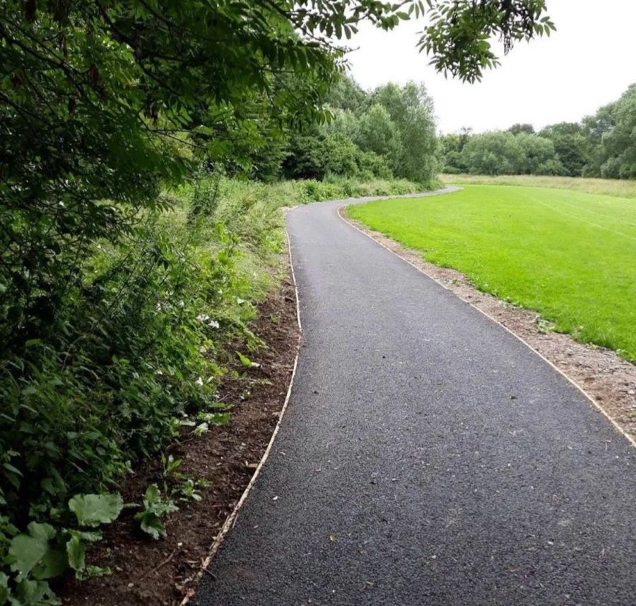 Curved tarmac pathway running alongside a mown grass field