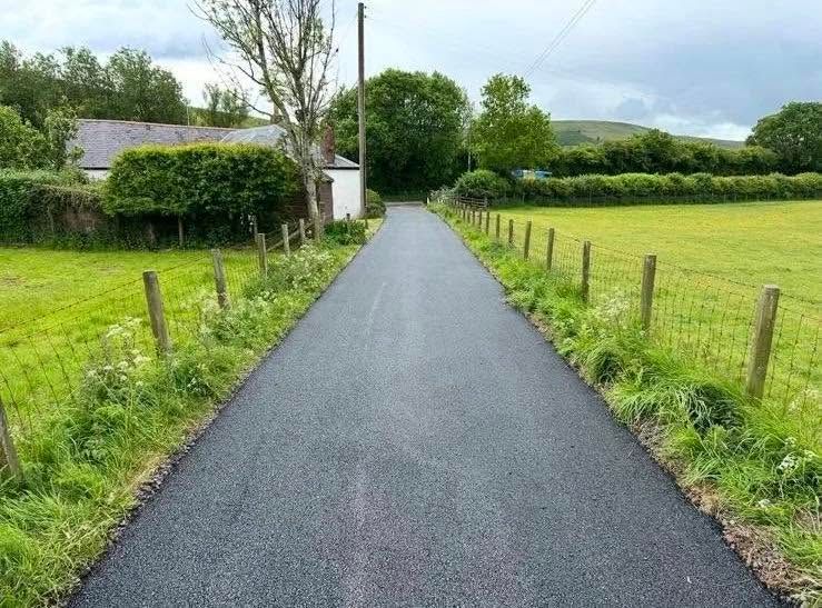 Newly surfaced private road running between fenced fields towards farm buildings