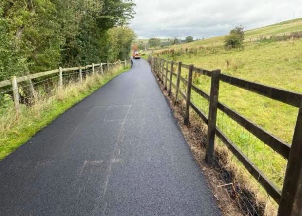 Newly surfaced private access road running between post and wire fencing through farmland