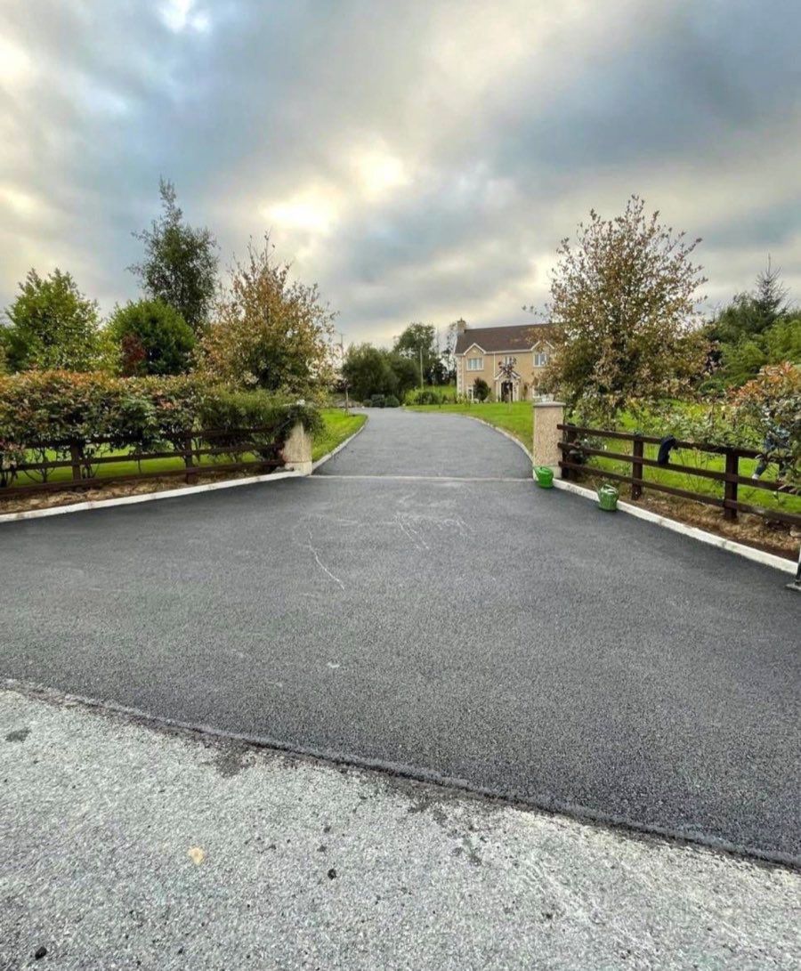 Tarmac driveway approach curving between hedges towards a stone house