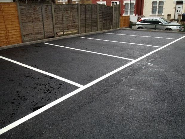 Freshly sprayed white parking bays on new tarmac behind a fenced boundary